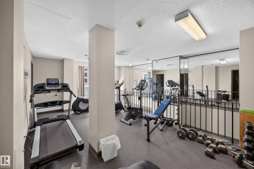 Fitness area featuring carpet tile flooring, a mirrored wall, and a black metal railing - #602 9725 106 St Nw, Edmonton, AB 