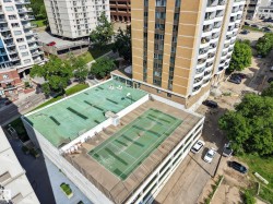 Rooftop tennis court with surrounding safety fencing, adjacent to a flat green roof area - 