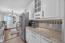Kitchen featuring white cabinetry, granite-finish countertops, and a subway tile backsplash with decorative accents - #602 9725 106 St Nw, Edmonton, AB 