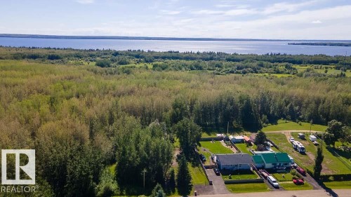 Expansive residential property featuring multiple structures, verdant lawns, and mature trees, with a large body of water and distant tree lines in the background - 4701 34 St., Rural Wetaskiwin County, AB 