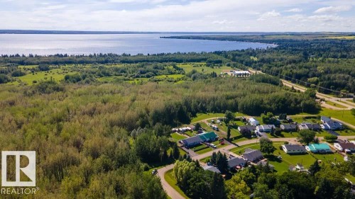 Expansive lakefront property featuring a broad body of water, extensive tree coverage, residential area, and open green spaces - 4701 34 St., Rural Wetaskiwin County, AB 
