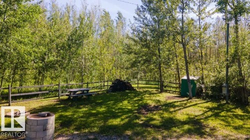 Expansive outdoor area featuring a wooden split-rail fence, mature trees, a picnic table, and a fire pit constructed from concrete blocks - 4701 34 St., Rural Wetaskiwin County, AB 