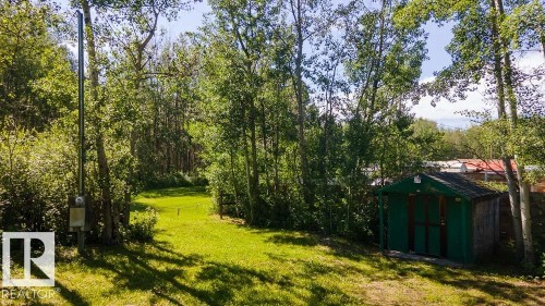 Expansive grassy area surrounded by mature trees, featuring a green storage shed with a dark shingle roof and a utility pole - 4701 34 St., Rural Wetaskiwin County, AB 