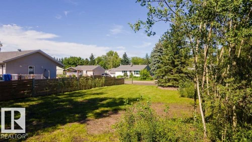 Expansive grassy lot featuring mature trees and a partial wood fence - 4701 34 St., Rural Wetaskiwin County, AB 