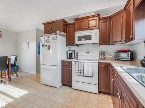 Kitchen featuring wood-finish cabinetry, white appliances including a refrigerator, range, and microwave, and a double basin sink - 57016 Range Road 13, Rural Barrhead County, AB - Indoor Photo Showing Kitchen
