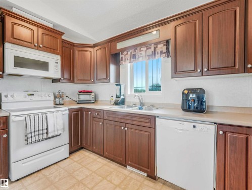 Kitchen featuring wood cabinetry with white knobs, white appliances, and light-toned countertops - 57016 Range Road 13, Rural Barrhead County, AB - Indoor Photo Showing Kitchen With Double Sink