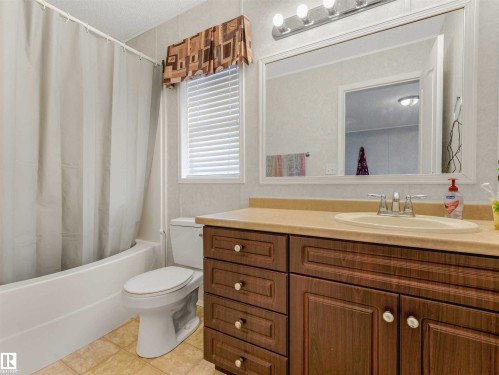 Bathroom featuring a white bathtub, ceramic wall tiling, wood-finish vanity with a built-in sink, and a framed mirror with overhead lighting - 57016 Range Road 13, Rural Barrhead County, AB - Indoor Photo Showing Bathroom