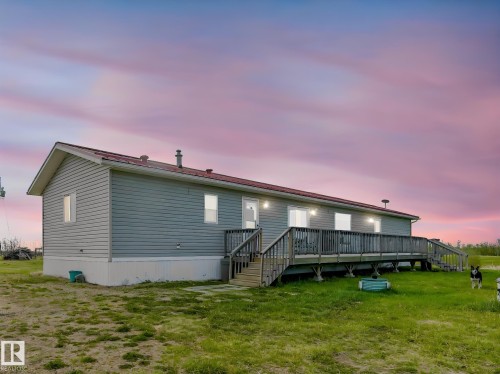 Single-story residence featuring light gray siding, a red metal roof, and a full-length wooden deck - 57016 Range Road 13, Rural Barrhead County, AB - Outdoor With Deck Patio Veranda