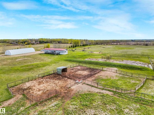 Expansive open acreage featuring multiple fenced enclosures, a large Quonset-style structure, and a single-story residence with a red roof and exterior decking - 57016 Range Road 13, Rural Barrhead County, AB - Outdoor With View