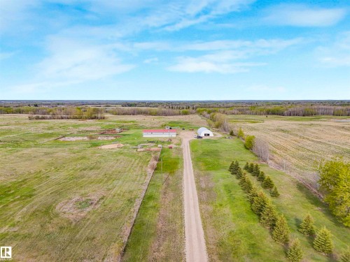 Expansive rural property featuring a long gravel driveway, a large red-roofed building, and an additional Quonset-style structure - 57016 Range Road 13, Rural Barrhead County, AB - Outdoor With View