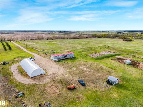 Expansive rural property featuring a long gravel driveway, a single-story residence with a covered porch, a large white hoop structure, a fenced animal enclosure, and multiple outbuildings across open fields - 57016 Range Road 13, Rural Barrhead County, AB - Outdoor With View