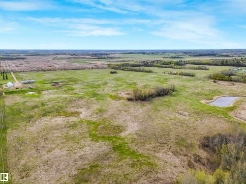 Expansive rural property featuring an established gravel driveway, multiple outbuildings including a hoop house, a natural pond, and cultivated fields - 57016 Range Road 13, Rural Barrhead County, AB - Outdoor With View