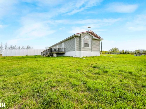 Siding exterior with a gable roofline, featuring an arched window, a wooden deck, and a spacious grassy area - 57016 Range Road 13, Rural Barrhead County, AB - Outdoor