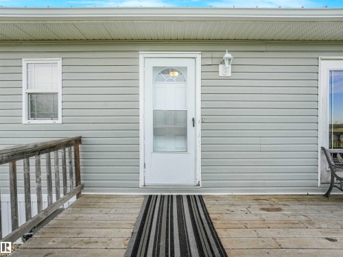 Light grey horizontal siding exterior featuring a white paneled entry door with a storm door, a white exterior light fixture, and a wooden ramp leading to the entrance - 57016 Range Road 13, Rural Barrhead County, AB - Outdoor With Exterior
