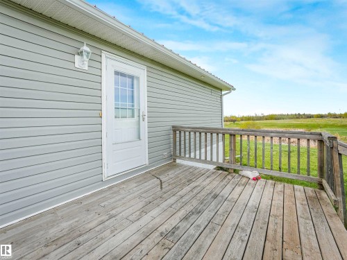 Outdoor wooden deck with railing, featuring a white exterior door with window panes, light gray siding, and an exterior wall lantern - 57016 Range Road 13, Rural Barrhead County, AB - Outdoor With Deck Patio Veranda With Exterior