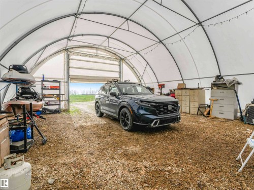 Spacious arched structure featuring a roll-up door, gravel flooring, interior lighting, and exposed metal framing - 57016 Range Road 13, Rural Barrhead County, AB - Indoor Photo Showing Garage