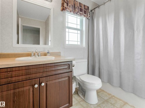 Bathroom featuring a wood-finish vanity with a light-toned countertop, a rectangular mirror, a white toilet, and a window with decorative valance - 57016 Range Road 13, Rural Barrhead County, AB - Indoor Photo Showing Bathroom