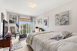 Light-colored bedroom featuring wall-to-wall carpeting, a large window with a bamboo blind, and a glass-paneled door opening to a balcony - 
