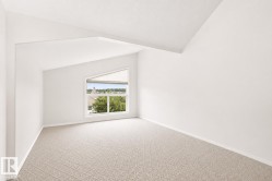 Spacious room featuring a large geometric window, textured carpeting, crisp white walls, and an angled ceiling line - 
