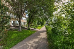 Paved pathway bordered by manicured lawn and mature trees, featuring a multi-story building with balconies and numerous windows - 