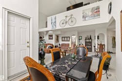 Open-concept interior featuring a dining area with ornate chair backs, a loft space, white walls, and arched doorways - 