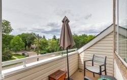 Balcony with beige vinyl siding, white railing, and a window with a brick surround - 