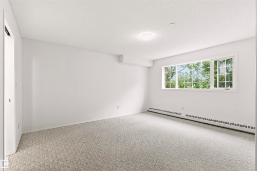 Carpeted room with a multi-pane window, baseboard heating, ceiling-mounted light fixture, and white wall finishes - #201 14 Mission Av, St. Albert, AB - Indoor Photo Showing Other Room