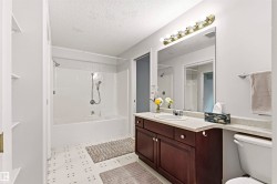 Bathroom featuring a tub/shower combination, dark wood-finish vanity with an integrated sink, broad wall-mounted mirror, and overhead vanity lighting - 