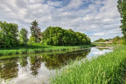 Waterfront property featuring a calm canal, lush green vegetation, mature trees, and a distant bridge - 