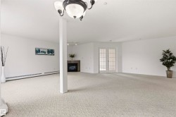 Expansive carpeted room featuring a ceiling-mounted light fixture, French doors with divided lites, a built-in fireplace with a stone surround, and baseboard heating - 