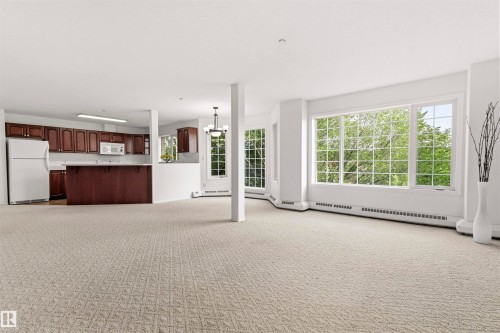 Expansive living area featuring large picture windows, patterned carpeting, and white walls - #201 14 Mission Av, St. Albert, AB - Indoor