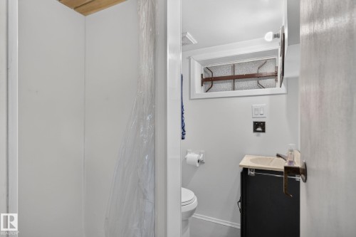 Bathroom featuring a white toilet, black vanity with a light-colored countertop, and a shower area with white walls - 12703 122 Street Nw, Edmonton, AB 