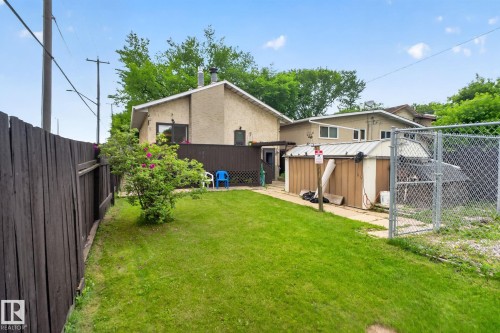 Expansive backyard featuring a lush lawn, mature shrubbery, a wood privacy fence, and a chain-link fence with a gate - 12703 122 Street Nw, Edmonton, AB 