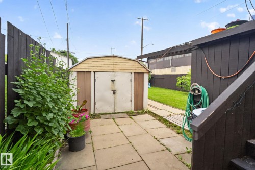 Paved patio area featuring a detached storage shed with double doors, wood-finish siding, and a gabled roof - 12703 122 Street Nw, Edmonton, AB 