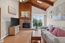 Living area featuring vaulted wood-paneled ceilings with exposed beams, a brick fireplace with a wood-paneled accent wall, wood-finish flooring, a skylight, and sliding glass doors opening to the exterior - 12703 122 Street Nw, Edmonton, AB 