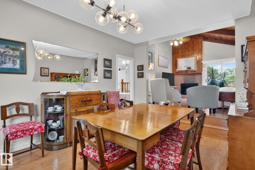 Open-concept dining area featuring wood-finish flooring, a modern multi-bulb chandelier, and an expansive wall mirror - 12703 122 Street Nw, Edmonton, AB 