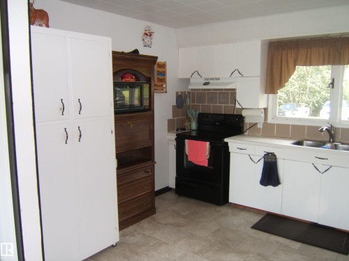 Kitchen featuring white cabinetry, a black electric range, a double basin sink, neutral tile flooring, and a tiled backsplash - 543016 Rng Rd 122, Rural Two Hills County, AB - Indoor Photo Showing Kitchen With Double Sink
