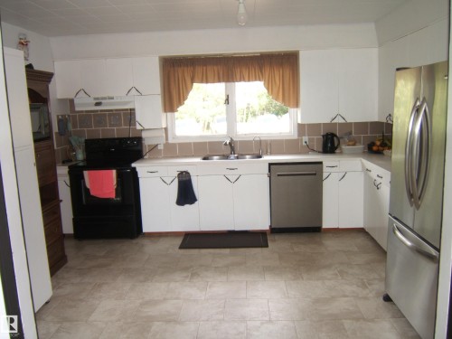 Bright kitchen featuring white cabinetry, light countertops, a tile backsplash, and a window above the sink - 543016 Rng Rd 122, Rural Two Hills County, AB - Indoor Photo Showing Kitchen With Double Sink