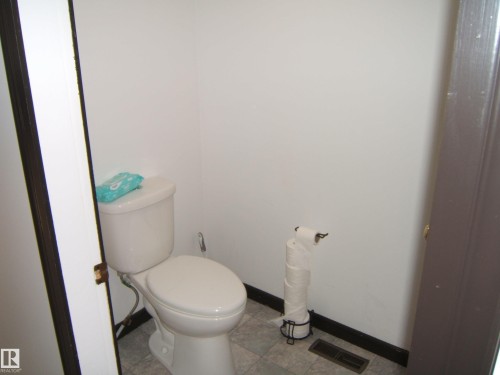 White porcelain toilet with a dark baseboard trim and light-colored floor tiling - 543016 Rng Rd 122, Rural Two Hills County, AB - Indoor Photo Showing Bathroom