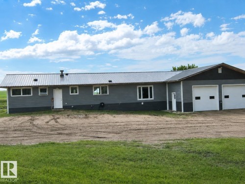 Exterior featuring gray siding with a dark gray foundation, a metal roof, and an attached two-car garage with white paneled doors - 543016 Rng Rd 122, Rural Two Hills County, AB - Outdoor