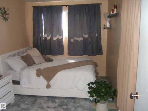 Bedroom featuring two windows with curtain rods, a wall-mounted shelving unit, and warm toned walls - 543016 Rng Rd 122, Rural Two Hills County, AB - Indoor Photo Showing Bedroom