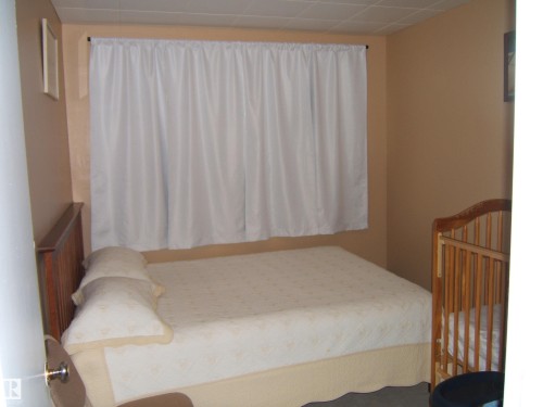 Window with white privacy curtain, tan wall color, wood-paneled headboard, and textured ceiling - 543016 Rng Rd 122, Rural Two Hills County, AB - Indoor Photo Showing Bedroom