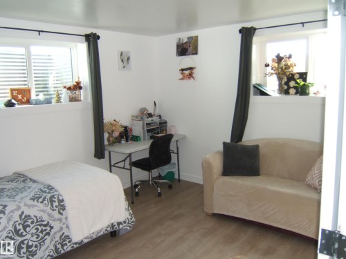 Bright interior space featuring wood-finish flooring, two windows with white blinds, and white baseboards - 543016 Rng Rd 122, Rural Two Hills County, AB - Indoor Photo Showing Bedroom