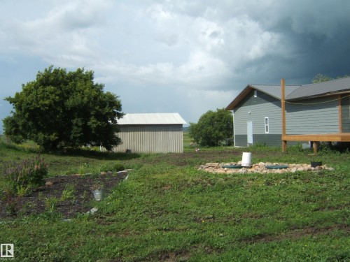 Gray siding residence with a wooden porch, accompanied by a detached outbuilding featuring a metal roof - 543016 Rng Rd 122, Rural Two Hills County, AB - Outdoor