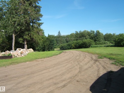Expansive outdoor space featuring a curving dirt road, mature trees, and a rock border - 543016 Rng Rd 122, Rural Two Hills County, AB - Outdoor