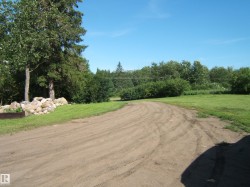 Expansive outdoor space featuring a curving dirt road, mature trees, and a rock border - 