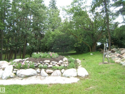 Expansive green lawn with a rock-lined garden bed featuring plantings - 543016 Rng Rd 122, Rural Two Hills County, AB - Outdoor