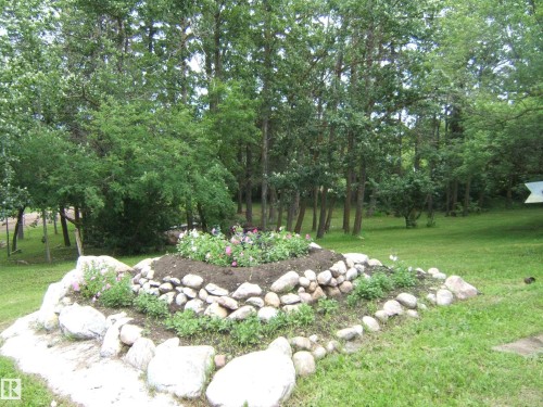 Expansive green space featuring a tiered rock garden with plantings, surrounded by mature trees and verdant foliage - 543016 Rng Rd 122, Rural Two Hills County, AB - Outdoor