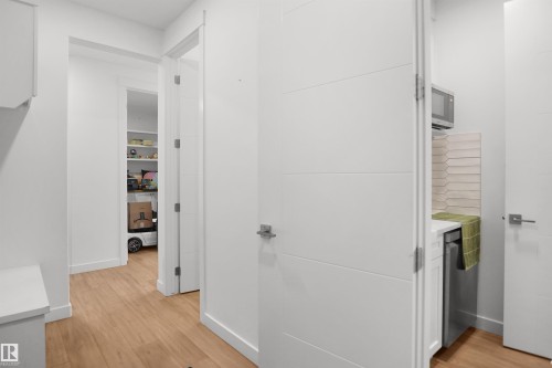Hallway with light wood-finish flooring, white walls, and modern white doors featuring horizontal paneling - 5802 Soleil Boulevard, Beaumont, AB 