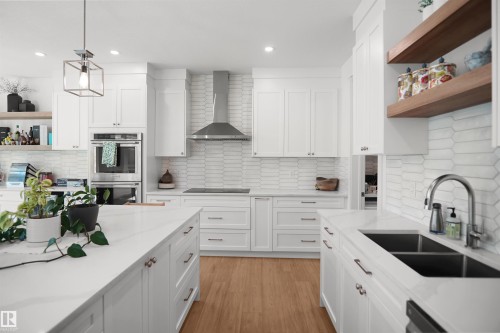 Gourmet kitchen with white cabinetry, wood-finish flooring, white countertops, stainless steel appliances, and a tiled backsplash - 5802 Soleil Boulevard, Beaumont, AB 